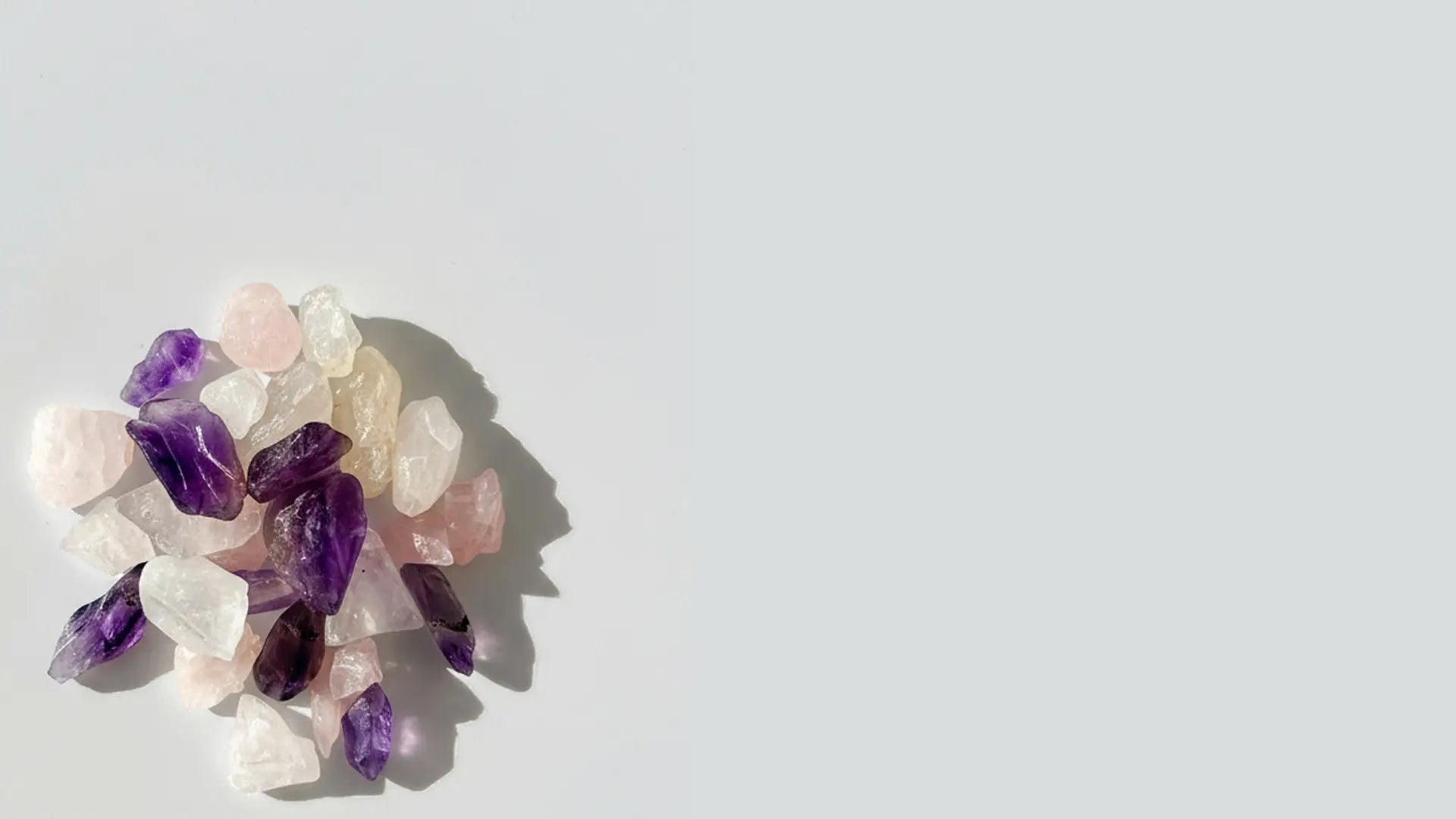 Ameythst, Clear Quartz, and Rose Quartz crystals on a light gray background