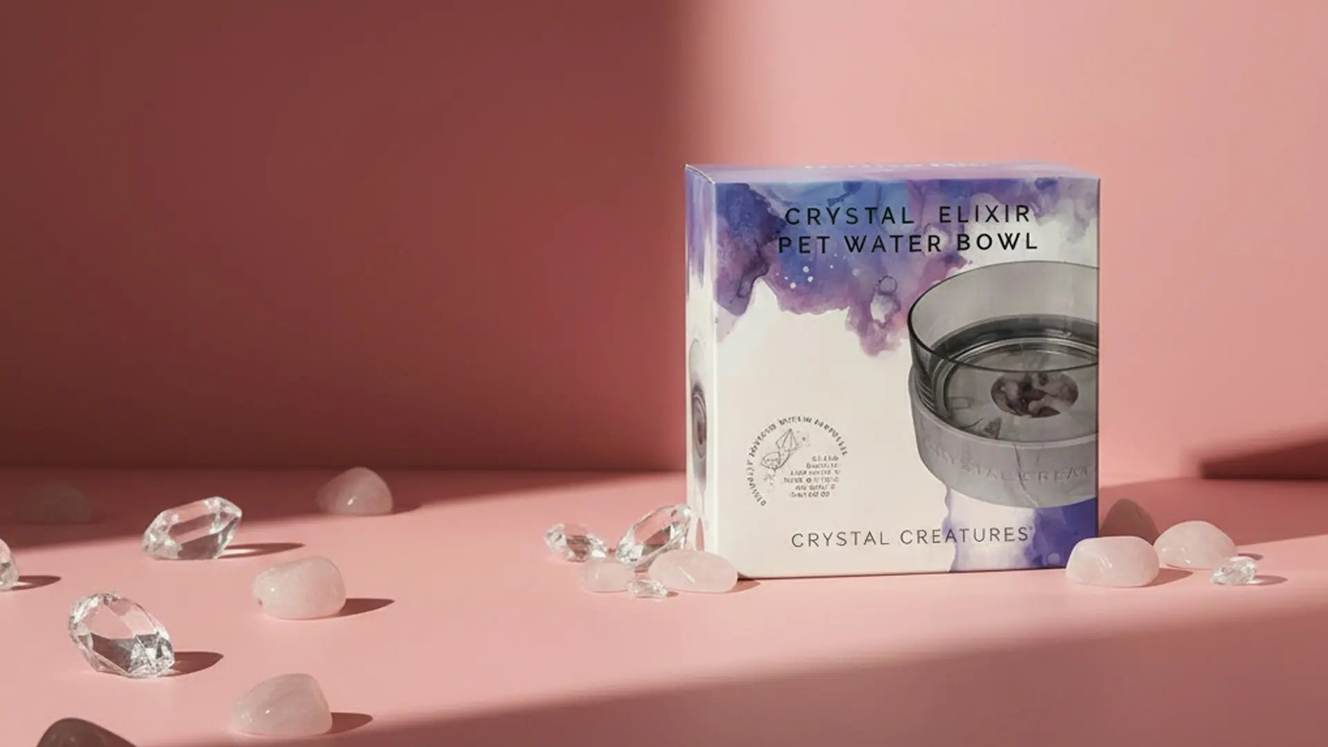 Box for 'Crystal Elixir Pet Water Bowl' with decorative stones on a pink background